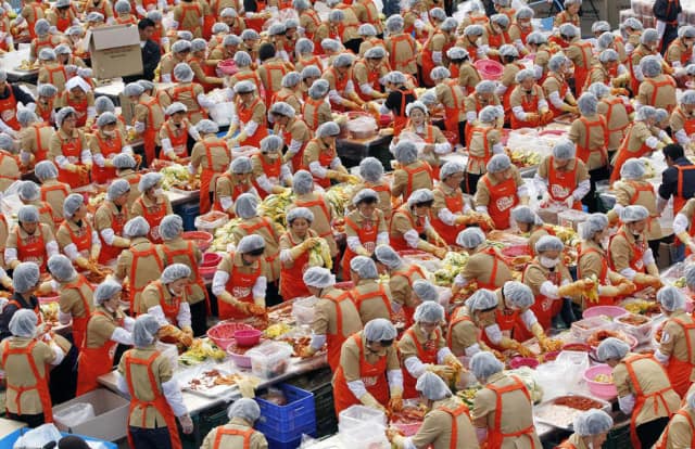 Annual Kimchi Festival with several people in clear head caps and orange aprons making kimchi. | MakeSauerkraut.com