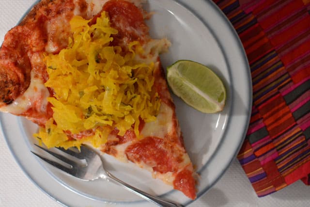 A white plate under Hawaiian Sauerkraut as a pizza topping and a metal fork at the side. | MakeSauerkraut.com