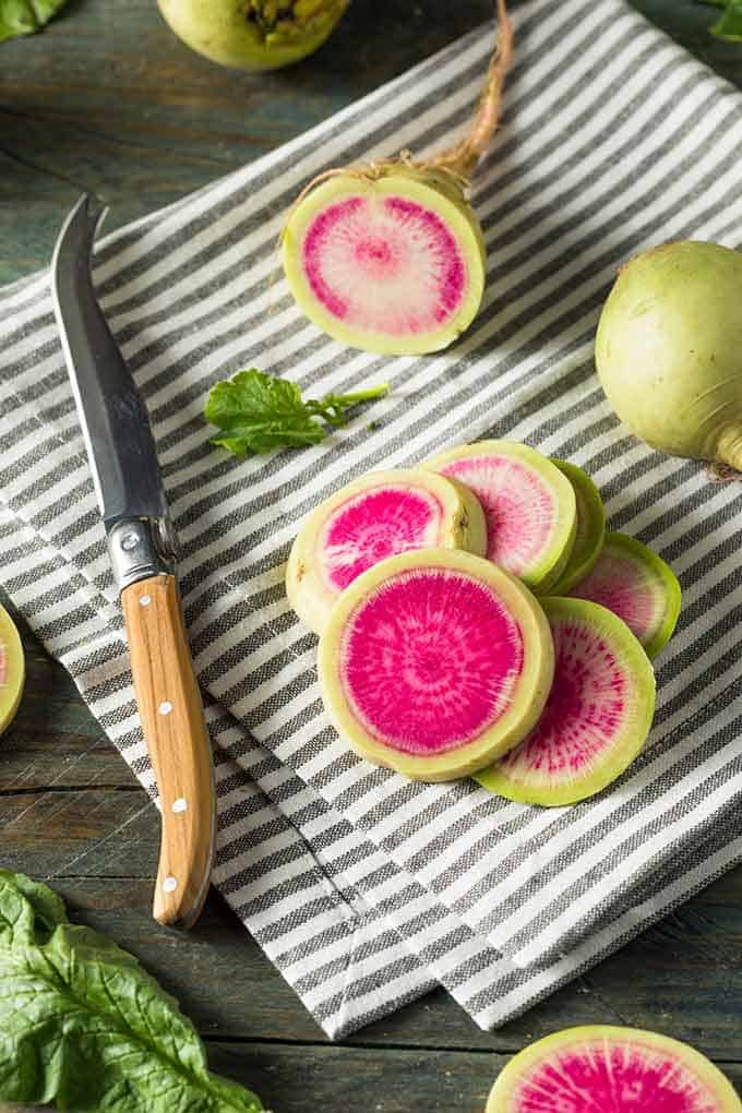 Sliced watermelon radish with small knife over a black and white striped cloth. | MakeSauerkraut.com