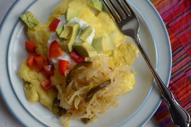 Scrambled eggs on white plate topped with spicy Kimchi sauerkraut and sour cream and a metal fork on the side. | MakeSauerkraut.com