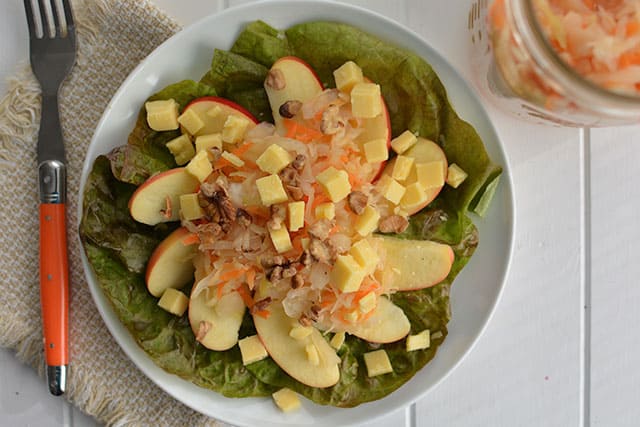 Ginger Garlic Sauerkraut salad with some sliced apples, toasted and chopped walnuts and cubed cheddar cheese in a white plate with a fork to the left. | MakeSauerkraut.com