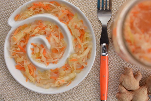 Ginger Garlic Sauerkraut in a swirly white plate and a metal fork with orange handle at the side. | MakeSauerkraut.com