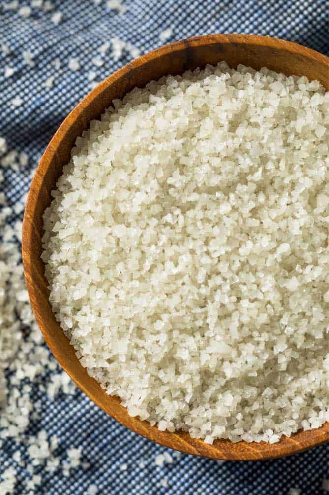 Gray sea salt inside a wooden bowl over blue cloth. | MakeSauerkraut.com