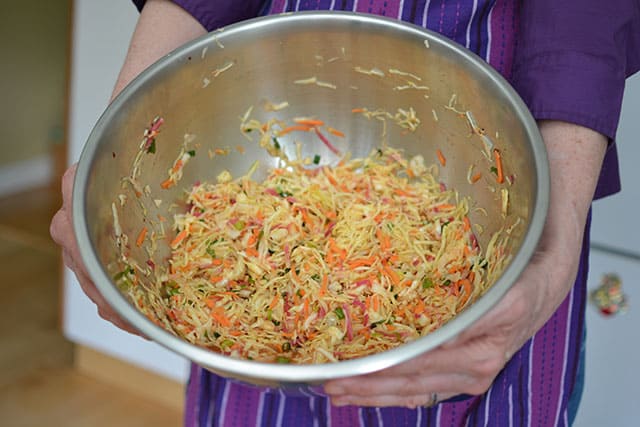 Kimchi Style Sauerkraut Recipe Sauerkraut mixture brined inside a big metal bowl and held by the front of a person in two hands. | MakeSauerkraut.com