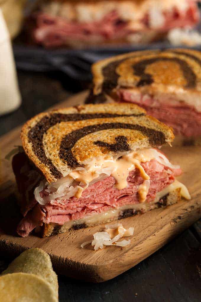 A bite-sized Reuben sandwich with a layers of sauerkraut in the middle on top of a wooden chopping board. | MakeSauerkraut.com