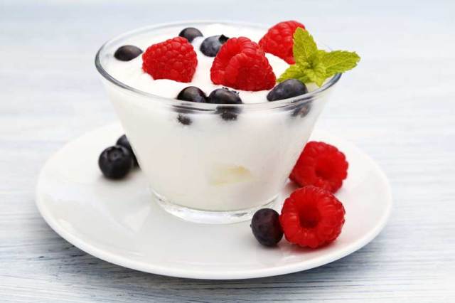 Yogurt in a small cup over white saucer with fresh raspberries and blueberries. | MakeSauerkraut.com