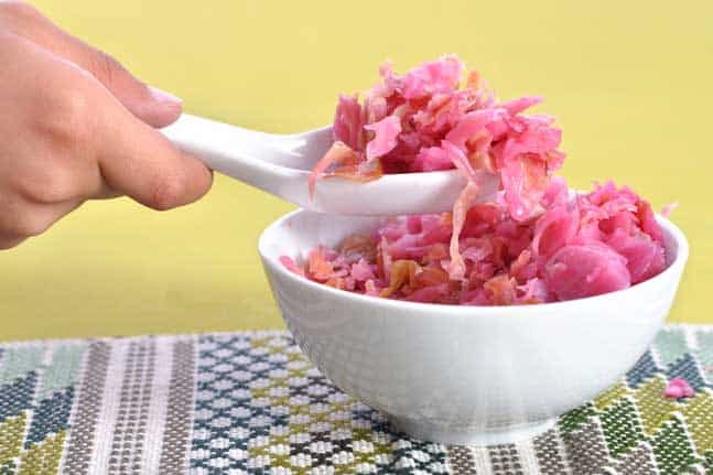 White bowl filled with sauerkraut and a hand holding a spoon scooping out a portion. | MakeSauerkraut.com