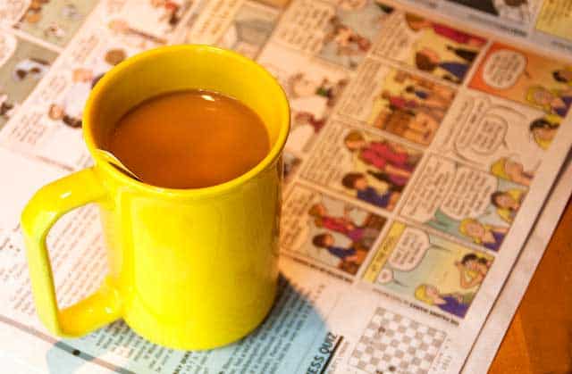 Yellow cup of morning tea over an opened magazine. | MakeSauerkraut.com