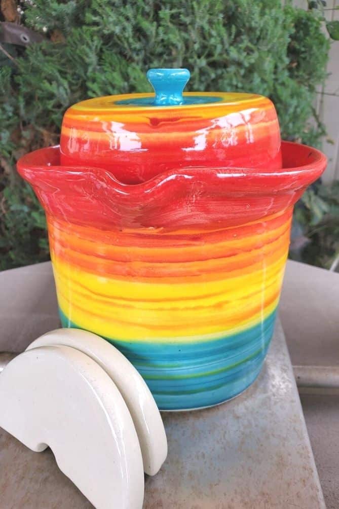 Rainbow colored crock with lid and weights. | MakeSauerkraut.com