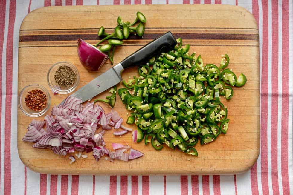 Chopped onions and green pepper on top of a chopping board with two small 
 bowls of herbs and a small knife. | MakeSauerkraut.com