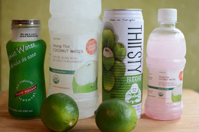 Different bottles of brands of coconut water and two limes in front of them. | MakeSauerkraut.com