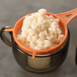 Milk kefir grains over an orange strainer over a black bowl. | MakeSauerkraut.com