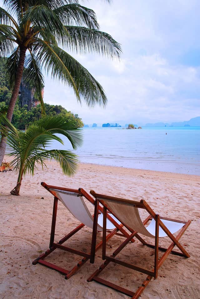 Tropical white sad beach with tow lounge chairs beside a small palm tree. | MakeSauerkraut.com