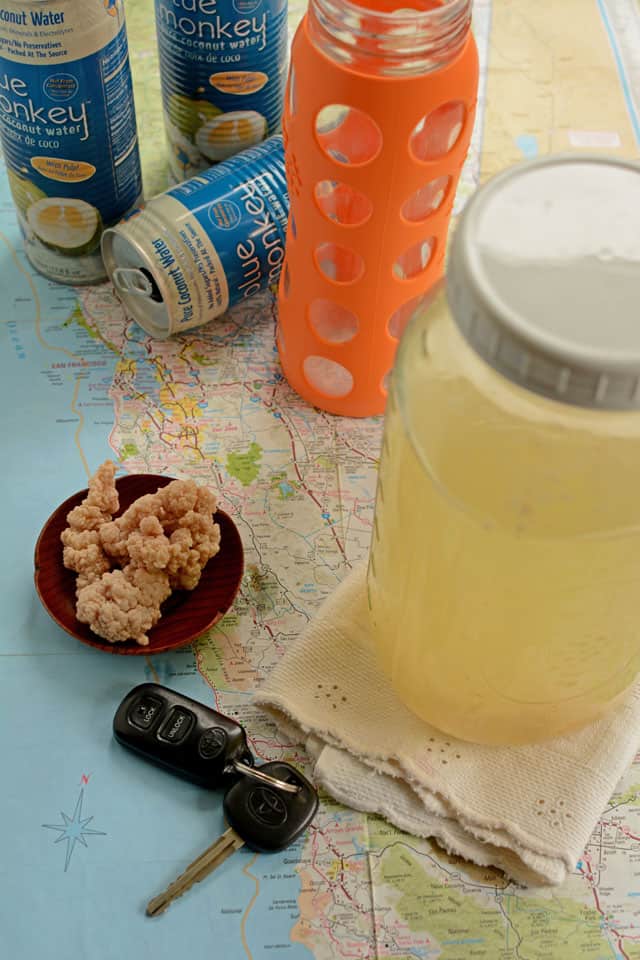 Jar of coconut water of white table cloth, car keys, and milk kefirs in a saucer plate at the side, cans and bottles at the background. | MakeSauerkraut.com