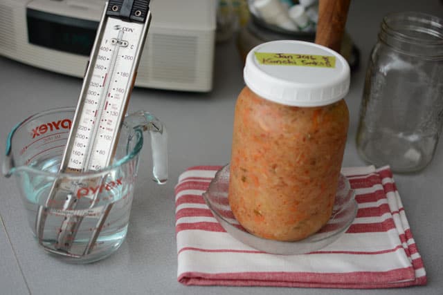 A probe thermometer in a measuring cup with water beside a jar of sauerkraut. | MakeSauerkraut.com