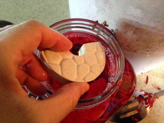 A hand holding stoneware clay fermentation weight by Tamarack Stoneware over an unopened glass jar of sauerkraut. | MakeSauerkraut.com