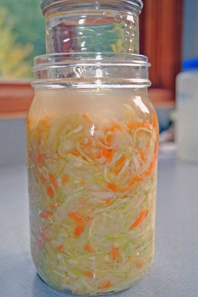 Smaller glass jar filled with water being inserted inside a jar filled with sauerkraut. | Makesauerkraut.com
