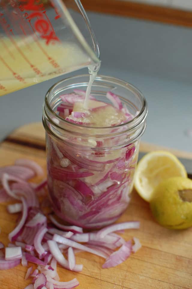 A measuring cup pouring brine over a jar of fermented onions. | MakeSauerkraut.com