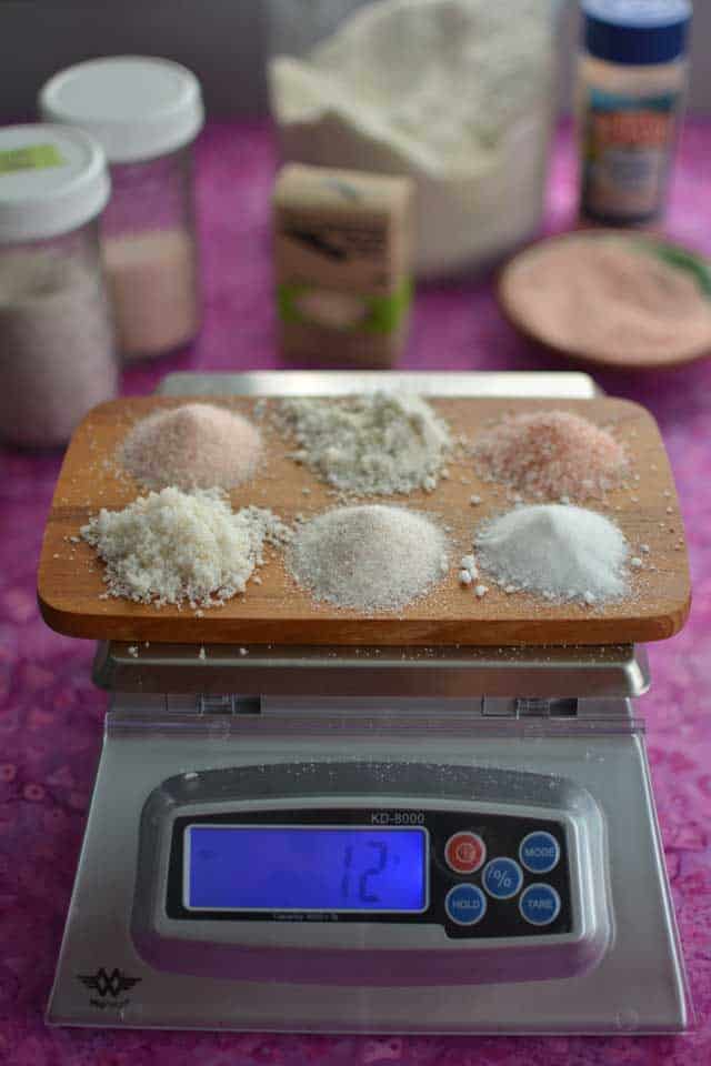 Six different salts on top of a wooden chopping board on top of a MyWeigh KD-8000. | MakeSauerkraut.com