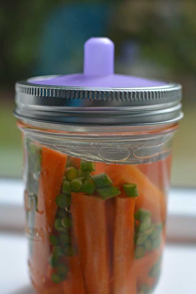 A jar of fermented carrots with a metal lid and Pickle Pipe attached. | MakeSauerkraut.com
