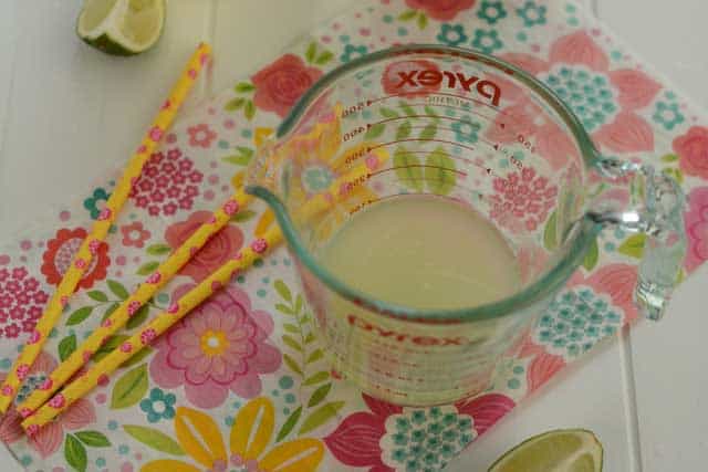 A glass measuring cup with a starter culture mixture, three yellow sticks with pink flower designs on the side in top of a flowery placemat. | MakeSauerkraut.com