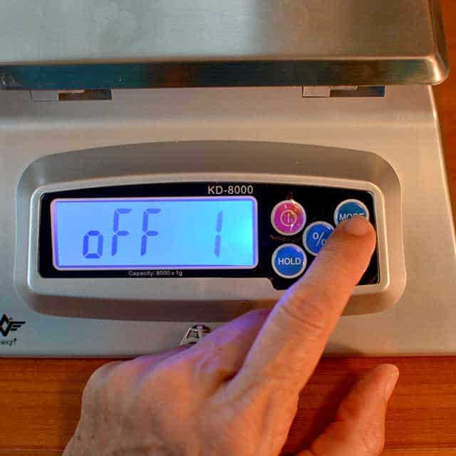 Fingers reaching to press "mode" on the MyWeigh KD-8000 digital scale with monitor showing "off 1". | MakeSauerkraut.com