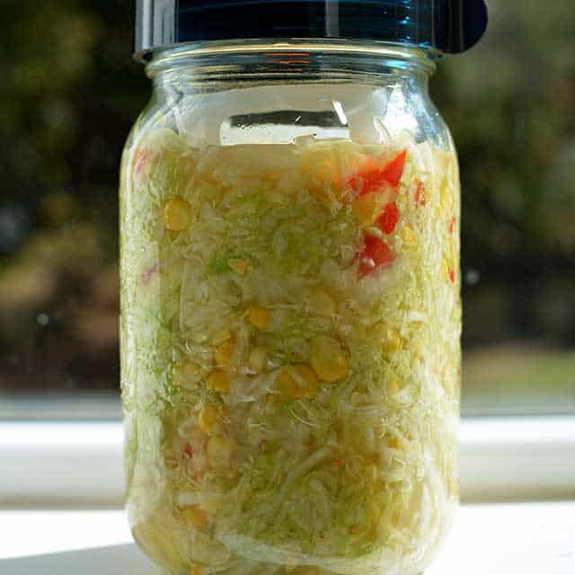 Front view of glass jar with sauerkraut with black lid. | MakeSauerkraut.com