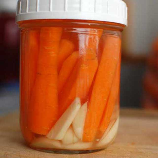 Jar of carrot sticks with brine and a white lid. | MakeSauerkraut.com
