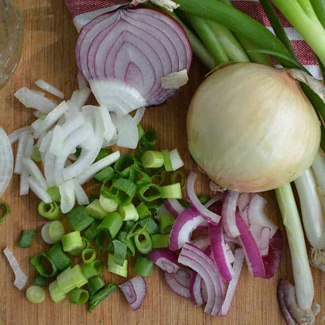 Chopped onions and spring onions with half of a while onion, whole white onion, and fresh spring onions in a wooden table top. | MakeSauerkraut.com