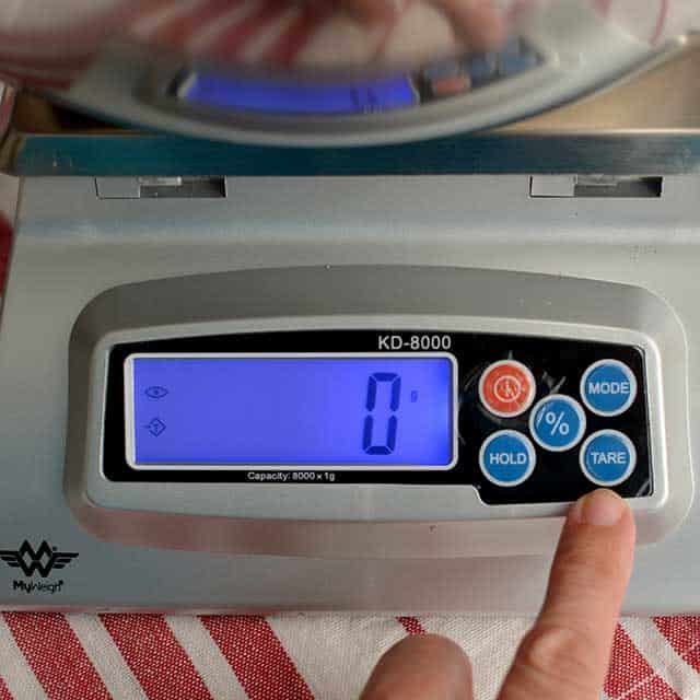 Fingers pressing "tare" on MyWeigh KD-8000 digital scale and the screen showing "0". | MakeSauerkraut.com