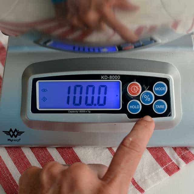 Front view of the MyWeigh KD8000 Digital Scale with the monitor showing "100.0" and an index finger touching the panel. | MakeSauerkraut.com
