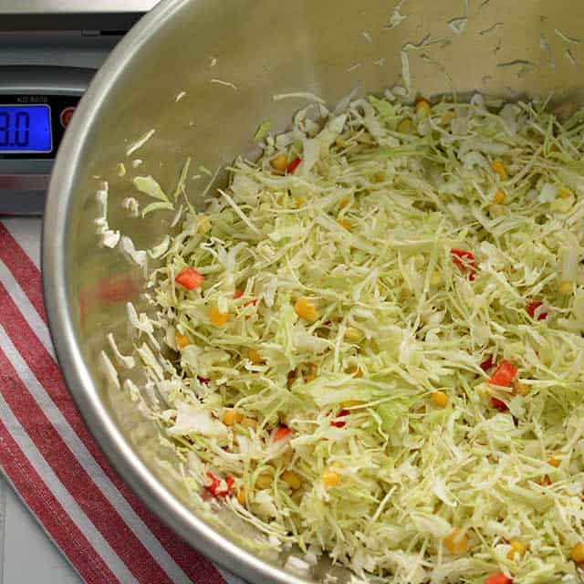 Metal bowl showing thinly sliced cabbage and other ingredients. | MakeSauerkraut.com