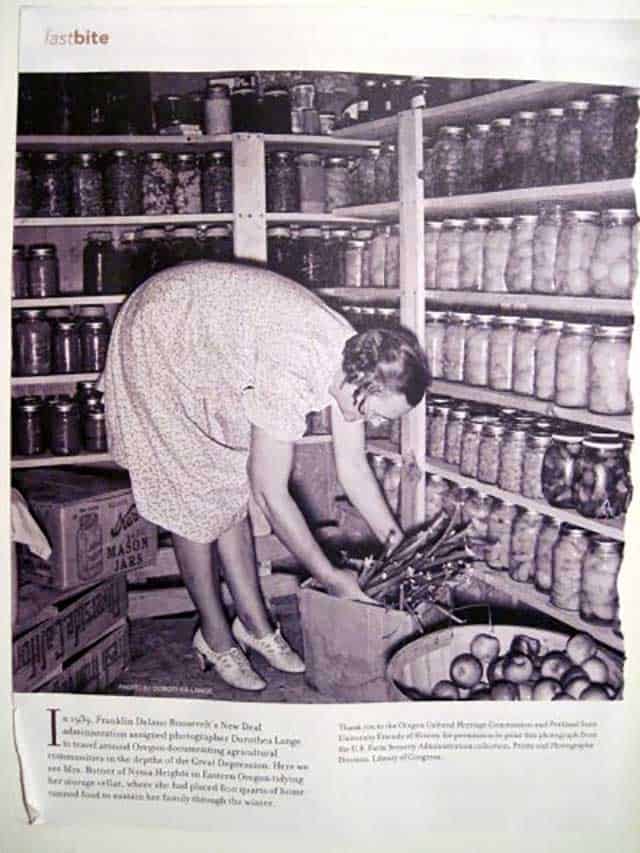 Old photo in a magazine from 1939 of a lady in a storage cellar bending down to arrange sticks in a box with rows of home-canned food on the shelves, boxes to the side and a barrel of apples. | MakeSauerkraut.com