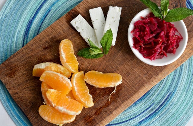 White bowl filled with Passion Pink sauerkraut with three slices of cheddar cheese to the side, and orange slices at the far end, all arranged on a wooden chopping board. | MakeSauerkraut.com