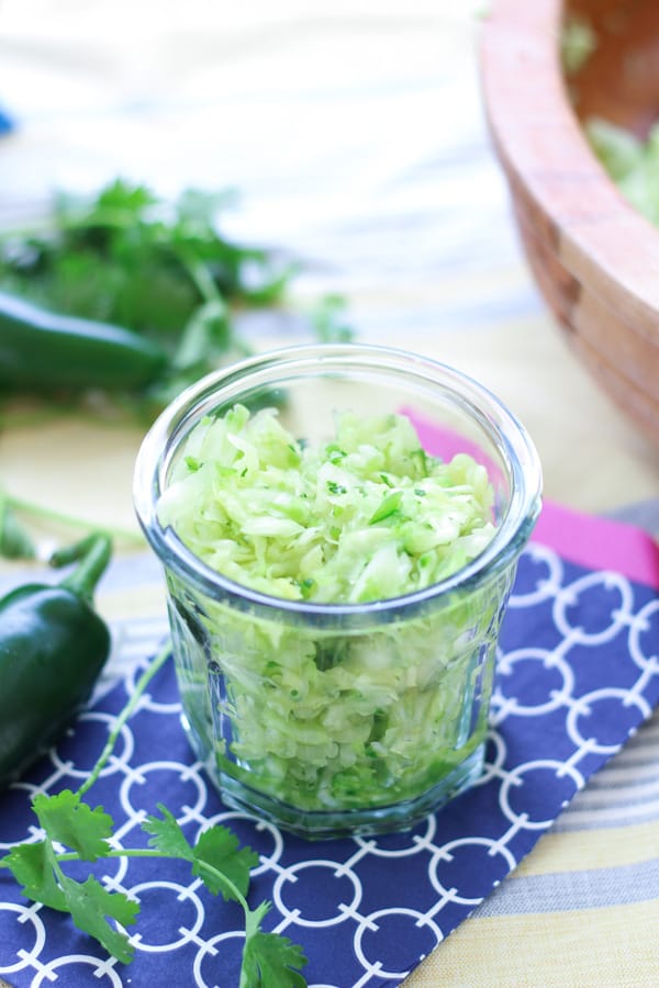 Jalapeno Cilantro Sauerkraut inside a small glass bowl over blue napkin. | MakeSauerkraut.com