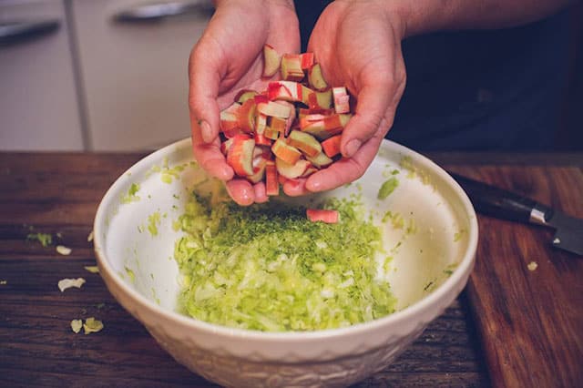 Two hands cupping a pile of sliced rhubarb to be added in a bowl filled with lime zest and other ingredients. | MakeSauerkraut.com