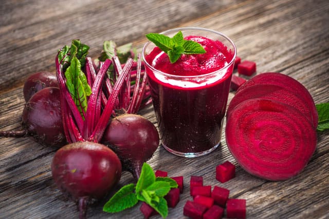 A glass with beetroot juice and sliced beetroots at the right side, and fresh, whole beetroots at the left. | MakeSauerkraut.com