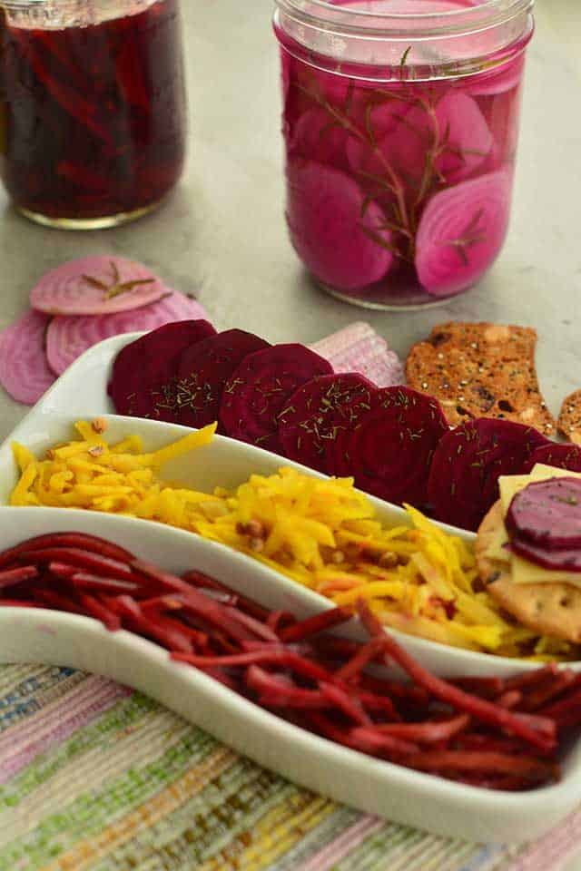 Image of white curved plate with three sections showing julienned beets, shredded yellow beets, sliced beets and biscuits and cheese as well as a glass jar filled with sliced beets and rosemary in brine. | MakeSauerkraut.com