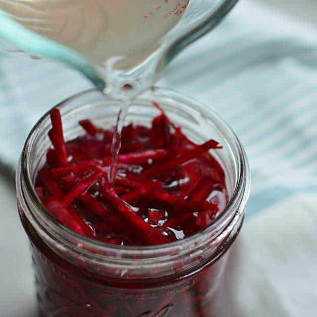 Pouring clear brine inside a glass jar with fresh red beets in Julienned cut. | MakeSauerkraut.com