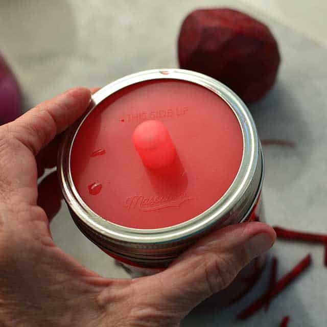 A hand closing the glass jar with an metal lid. | MakeSauerkraut.com