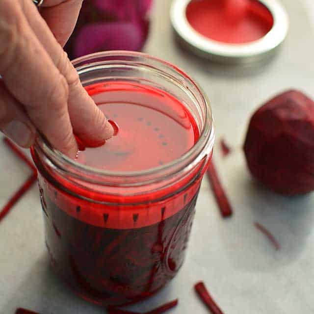 A hand adding the fermentation weight inside the glass jar with the fresh red beets inside. | MakeSauerkraut.com