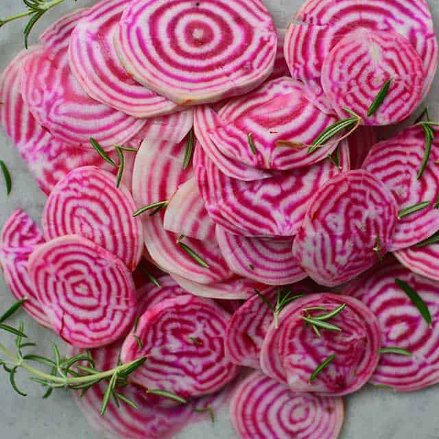 Pile of fresh beets cut in circles with white and red rings inside and some rosemary sprinkled on top. | MakeSauerkraut.com