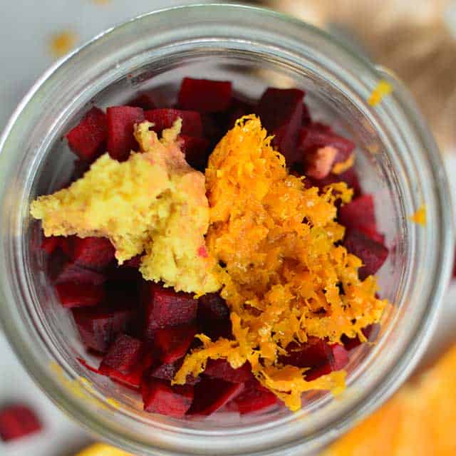 Top view of diced red beets and grated ginger on top inside a jar. | MakeSauerkraut.com