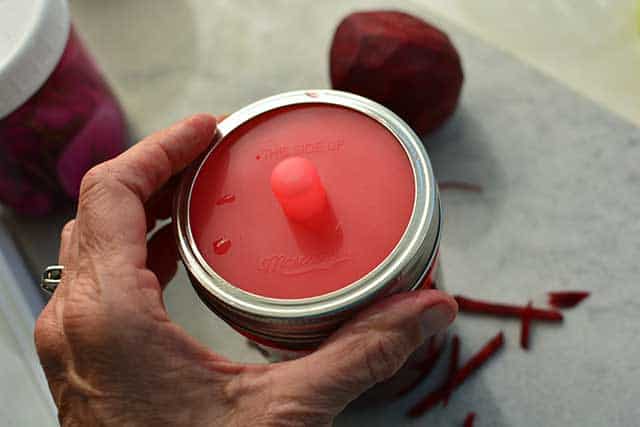 A hand holding the glass jar by the rim showing the pickle pip airlock lid. | MakeSauerkraut.com