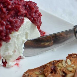 A white plate with goat cheese topped with fermented Cranberry-Orange Relish and crackers. | MakeSauerkraut.com