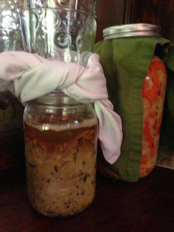 Jar of sauerkraut with white cloth over the lid with a brown brine. | MakeSauerkraut.com