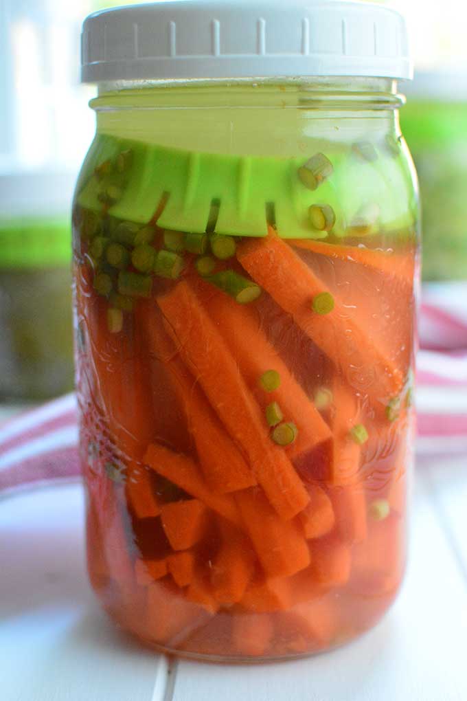 Glass jar with white lid filled with fermented carrots and green fermentation weight keeping vegetables below the brine. | MakeSauerkraut.com