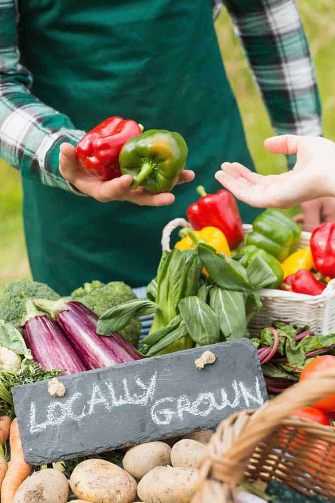 Farmer's stall with different vegetables and a hand reaching out for the green and red bell pepper in the hand of the farmer. | MakeSauerkraut.com