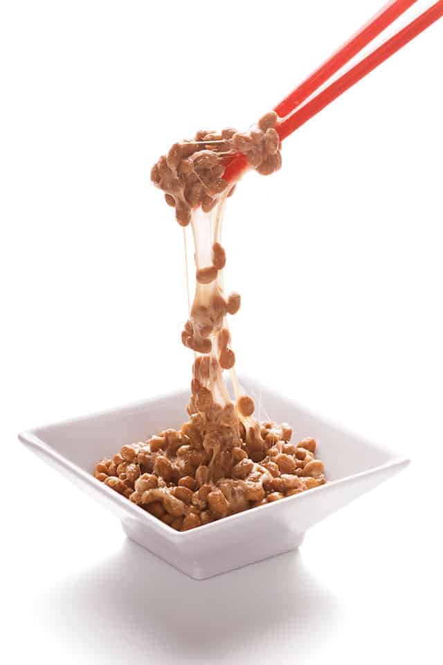 Natto, a Japanese soybean dish, in a square-shaped bowl and a line of Natto being stretched by chopsticks. | MakeSauerkraut.com