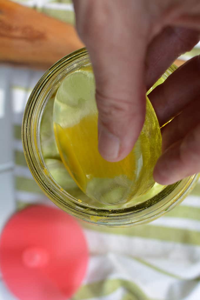 Hands inserting the Pickle Pebble fermentation weight by Mason Tops into a jar of sauerkraut. | MakeSauerkraut.com